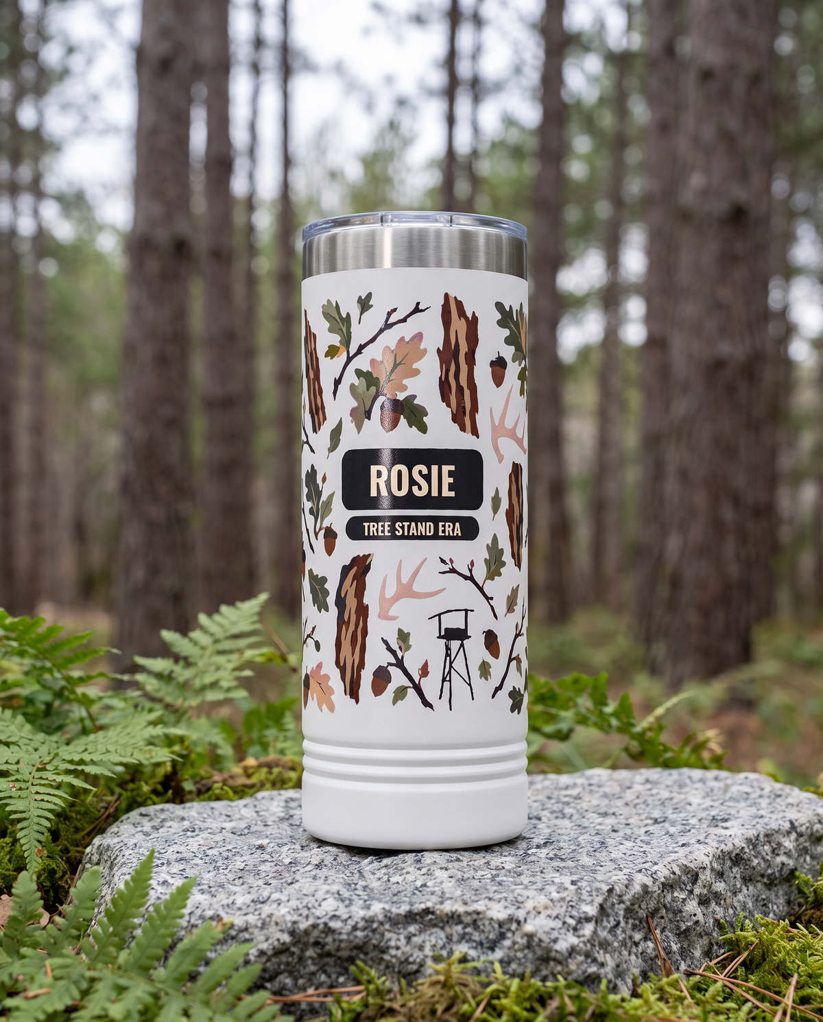 Heritage Bark Camo, Tree Stand Era wrap on a white 22oz Skinny tumbler personalized ROSIE, TREE STAND ERA, a granite boulder among ferns in a pine forest