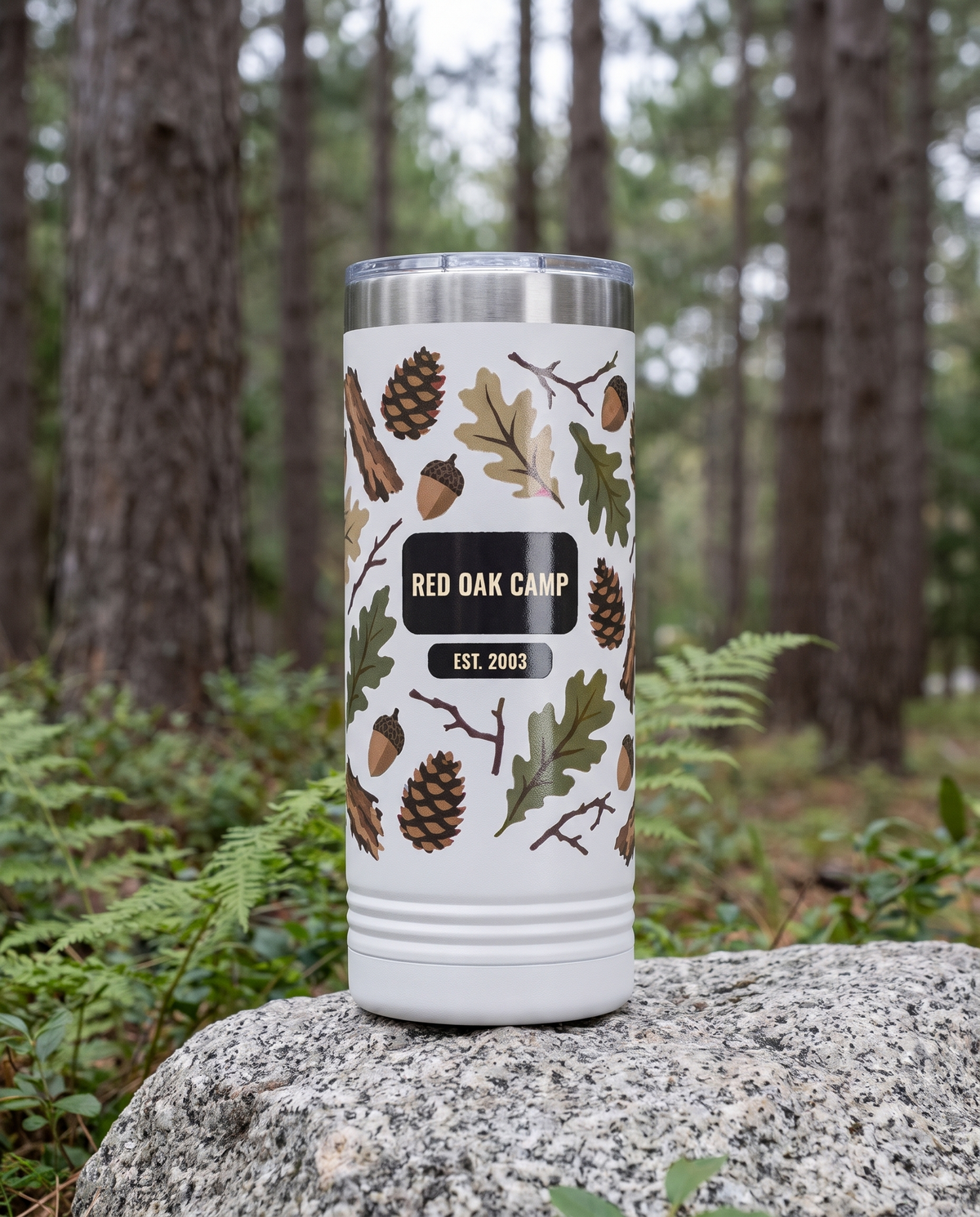 Heritage Bark Camo, Camp Name wrap on a white 22oz Skinny tumbler personalized RED OAK CAMP, EST. 2003, a granite boulder among ferns in a pine forest