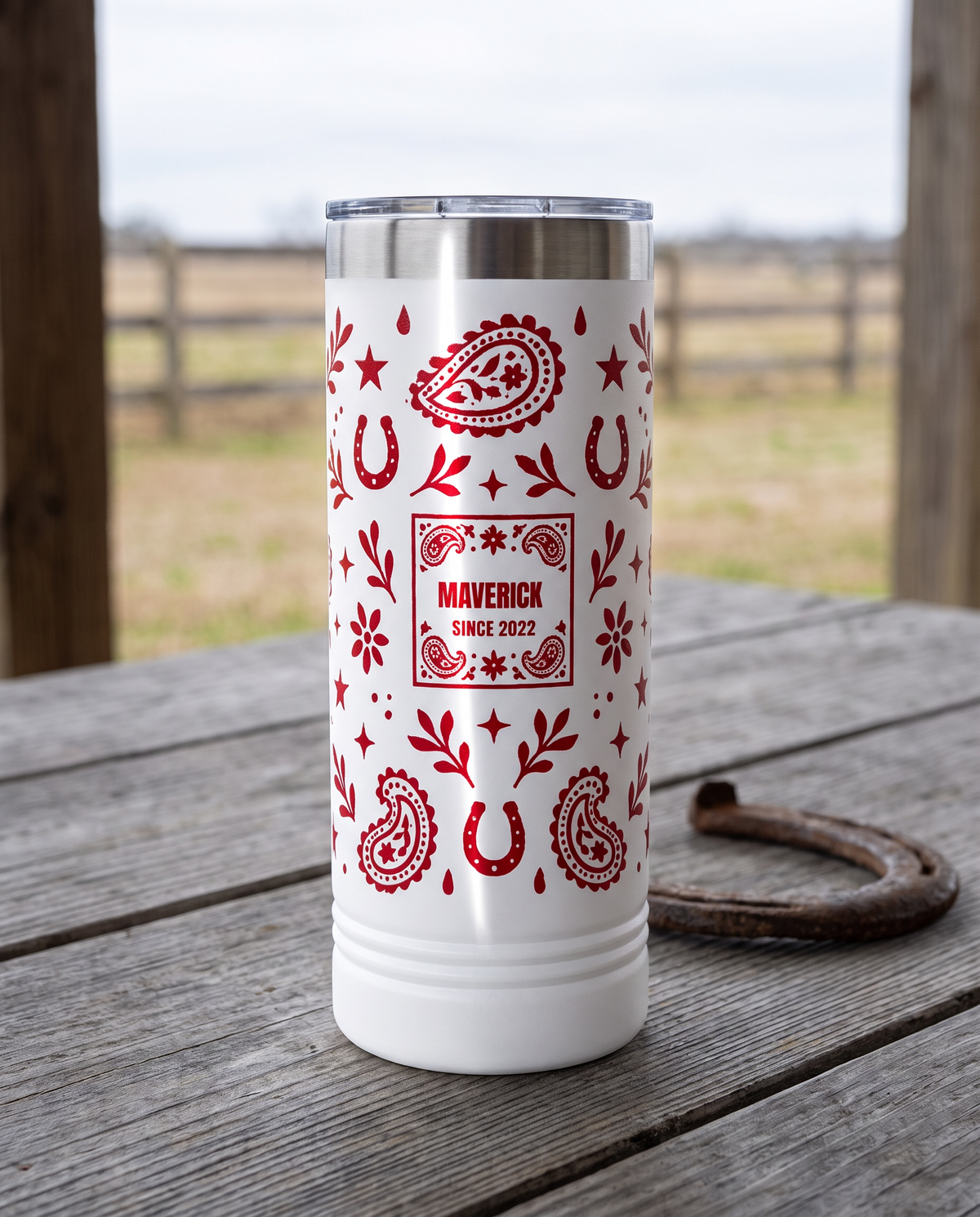 Bandana Paisley, Since Year wrap on a white 22oz Skinny tumbler personalized MAVERICK, SINCE 2022, a weathered barnwood table on a ranch porch