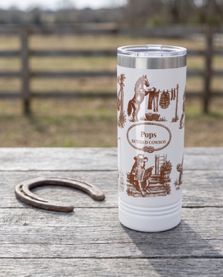 Western Toile, Retired Cowboy wrap on a white 22oz Skinny tumbler personalized POPS, RETIRED COWBOY, a weathered barnwood table on a ranch porch