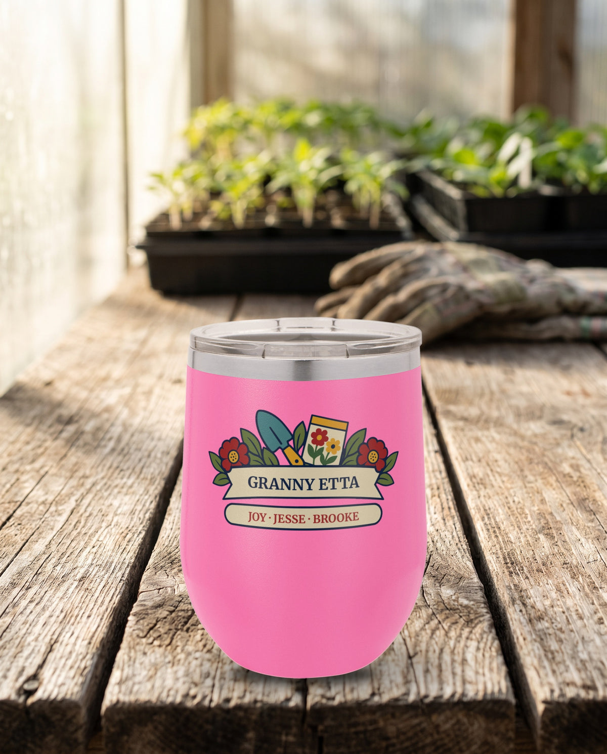 Seed Packet Garden, a garden scene in red, teal, gold, green and cream, outlined in navy, UV printed on the front of a 12oz stemless wine tumbler in Pink, sample name GRANNY ETTA