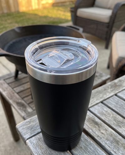 Clear slider lid on a black 20oz Ringneck tumbler, on a patio table by a fire pit