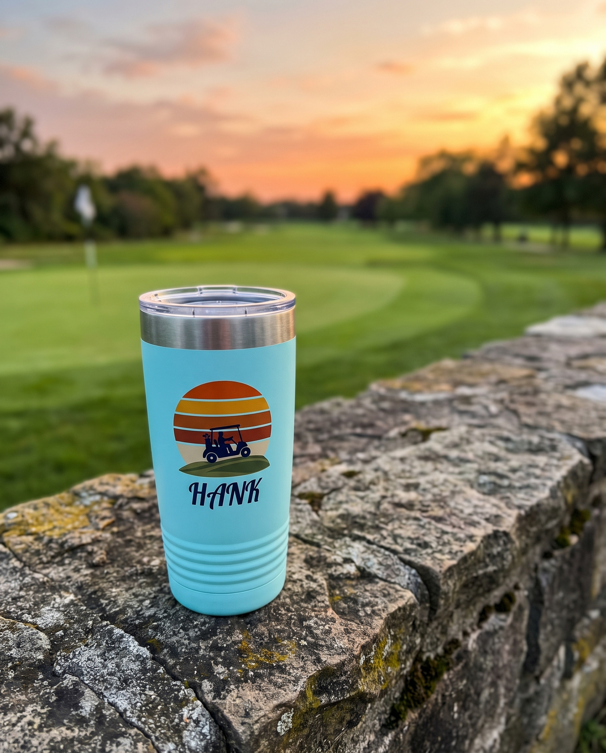 Retro Sunset Cart personalized golf tumbler on a stone wall by the 18th green at dusk