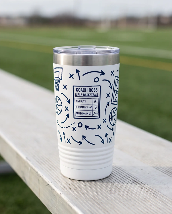 Coach Chalk Talk, Basketball wrap on a white 20oz tumbler personalized COACH ROSS, GIRLS BASKETBALL, three-quarter view showing the ribbed lower wall, a sideline bench beside an empty green sports field