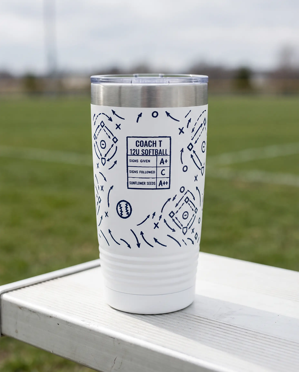 Coach Chalk Talk, Softball wrap on a white 20oz tumbler personalized COACH T, 12U SOFTBALL, a white bench outdoors beside an empty green sports field on an overcast day