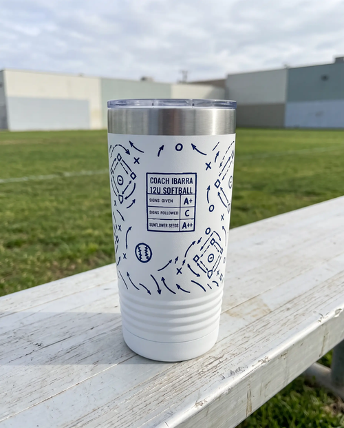 Coach Chalk Talk, Softball wrap on a white 20oz tumbler personalized COACH IBARRA, 12U SOFTBALL, three-quarter view showing the ribbed lower wall, a sideline bench beside an empty green sports field