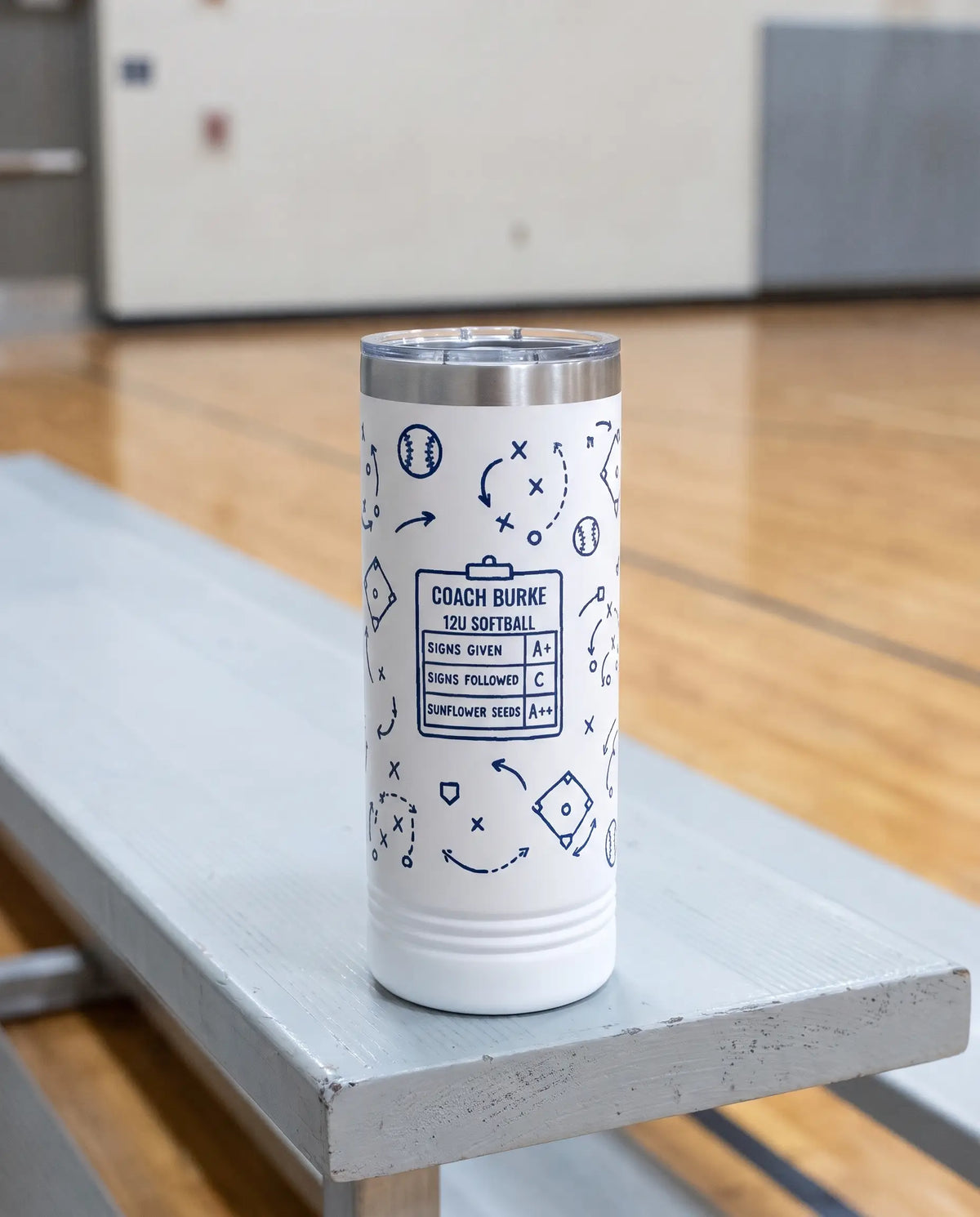 Coach Chalk Talk, Softball wrap on a white 22oz Skinny tumbler personalized COACH BURKE, 12U SOFTBALL, the pale gray bleacher bench of a school gym