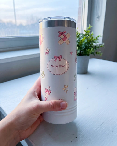 Bow Toss, Nurse wrap on a white 22oz Skinny tumbler personalized Nurse Chan, held in one hand, a white hospital break-room table by a window at dawn