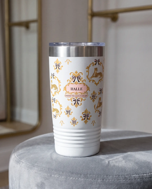 Cheetah Damask, Pickup Line wrap on a white 20oz tumbler personalized HALLE, three-quarter view showing the ribbed lower wall, a velvet ottoman in a boutique dressing room