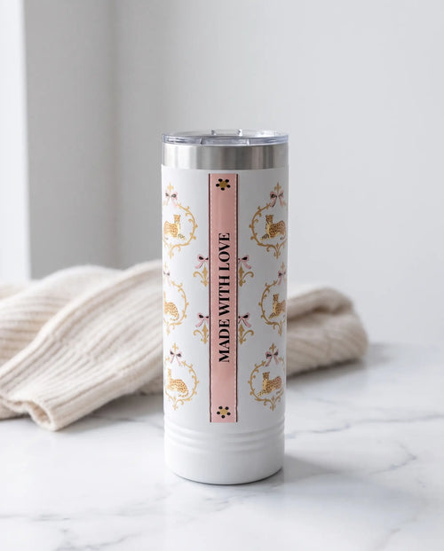 Back of a white 22oz Skinny tumbler with the Cheetah Damask wrap, the band reading MADE WITH LOVE, in a stylish bedroom