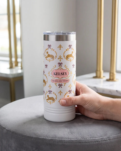 Cheetah Damask, The Boss wrap on a white 22oz Skinny tumbler personalized KELSEY, held in one hand, a velvet ottoman in a boutique dressing room