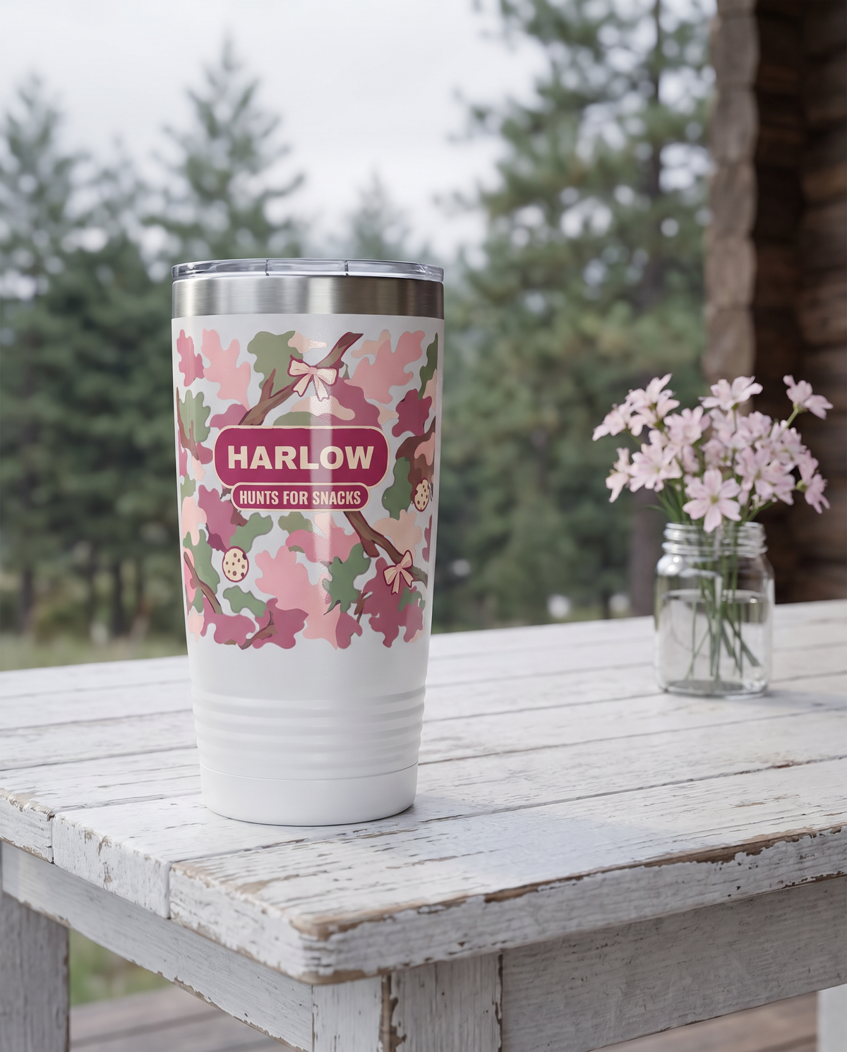 Blush Camo & Bows, Hunts for Snacks wrap on a white 20oz tumbler personalized HARLOW, HUNTS FOR SNACKS, a white-painted table on a cabin porch with pale pink wildflowers
