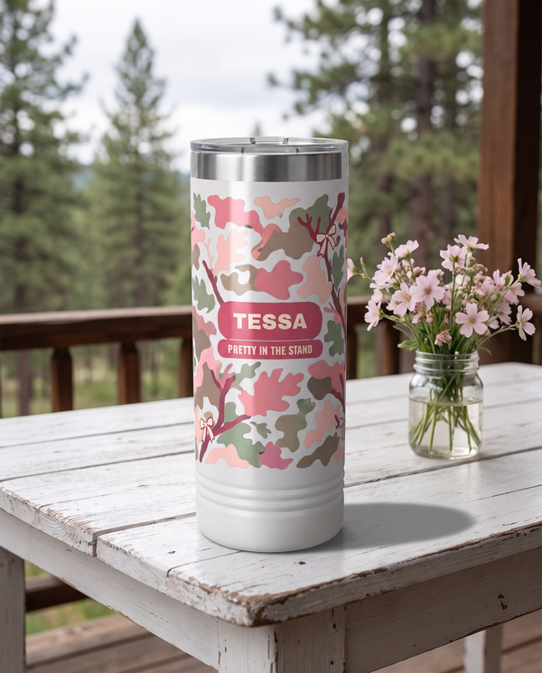 Blush Camo & Bows, Pretty in the Stand wrap on a white 22oz Skinny tumbler personalized TESSA, PRETTY IN THE STAND, a white-painted table on a cabin porch with pale pink wildflowers