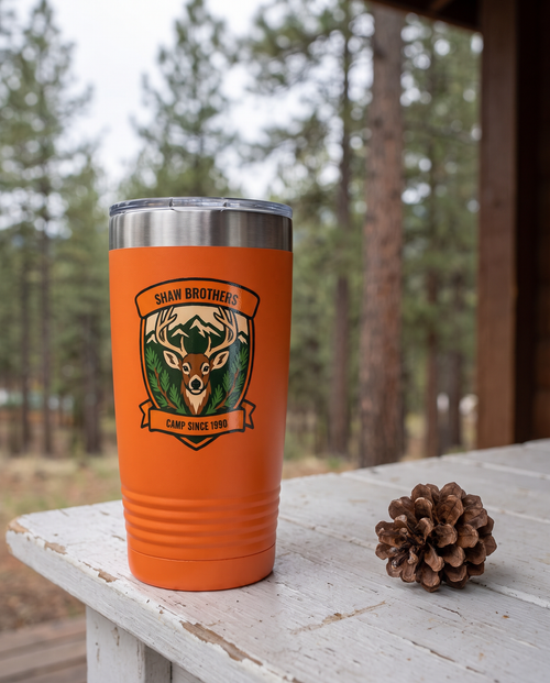 Deer Camp Patch, Buck Shield badge on an orange 20oz tumbler personalized SHAW BROTHERS, CAMP SINCE 1990, a white-painted table on a cabin porch