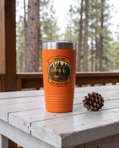 Deer Camp Patch, Deer Are Safe Here badge on an orange 20oz tumbler personalized PAPA'S CAMP, DEER ARE SAFE HERE, a white-painted table on a cabin porch