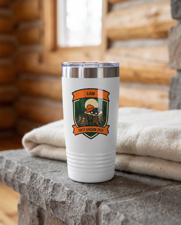 Deer Camp Patch, First Season badge on a white 20oz tumbler personalized LIAM, FIRST SEASON 2026, a stone hearth ledge in a log cabin