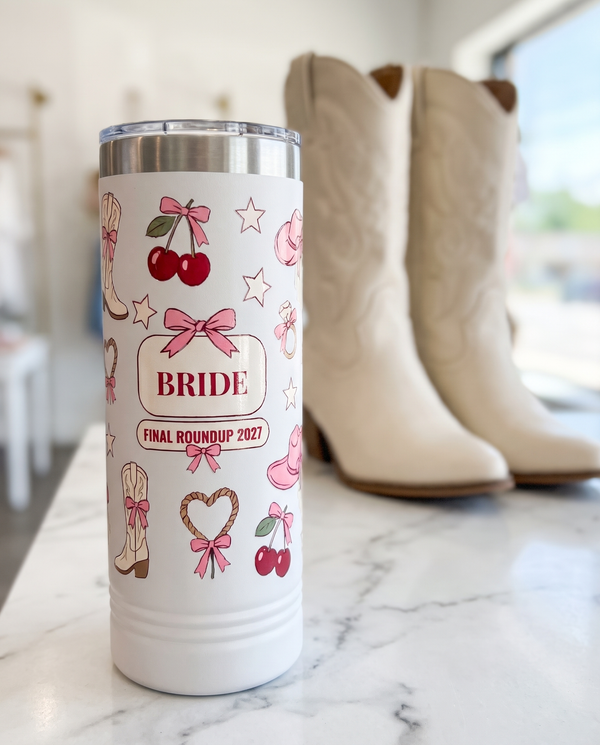 Coquette Cowgirl, Final Roundup wrap on a white 22oz Skinny tumbler personalized BRIDE, FINAL ROUNDUP 2027, a white marble vanity top in a bright boutique