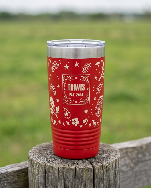 Bandana Paisley, Est. Year wrap on a red 20oz tumbler personalized TRAVIS, EST. 2016, a weathered fence post at a ranch