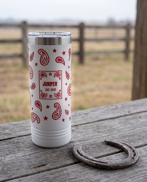Bandana Paisley, Est. Year wrap on a white 22oz Skinny tumbler personalized JUNIPER, EST. 2012, a weathered barnwood table on a ranch porch