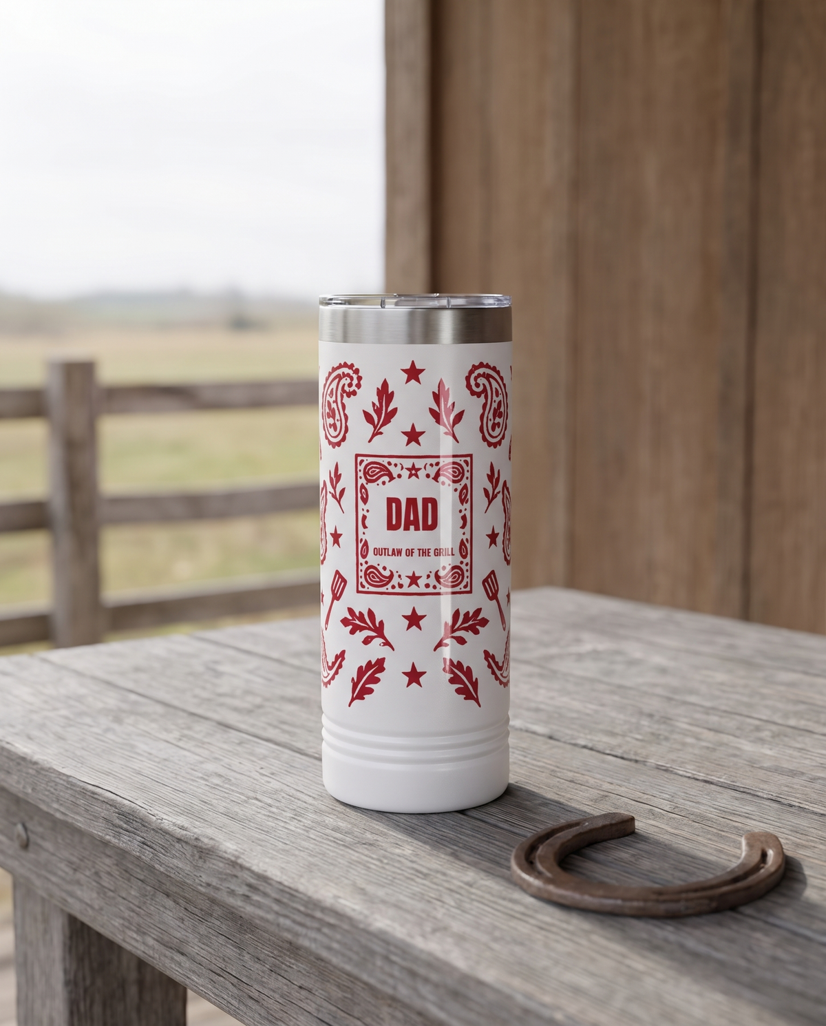 Bandana Paisley, Outlaw of the Grill wrap on a white 22oz Skinny tumbler personalized DAD, OUTLAW OF THE GRILL, a weathered barnwood table on a ranch porch