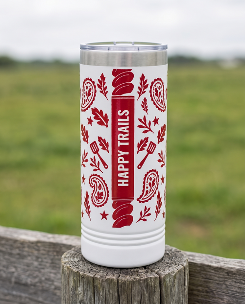 Back of a white 22oz Skinny tumbler with the Bandana Paisley, Outlaw of the Grill wrap, the band reading HAPPY TRAILS, a weathered fence post at a ranch