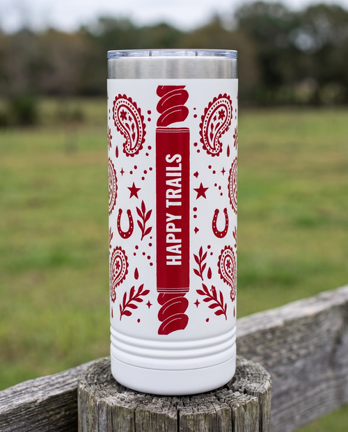 Back of a white 22oz Skinny tumbler with the Bandana Paisley, Since Year wrap, the band reading HAPPY TRAILS, a weathered fence post at a ranch
