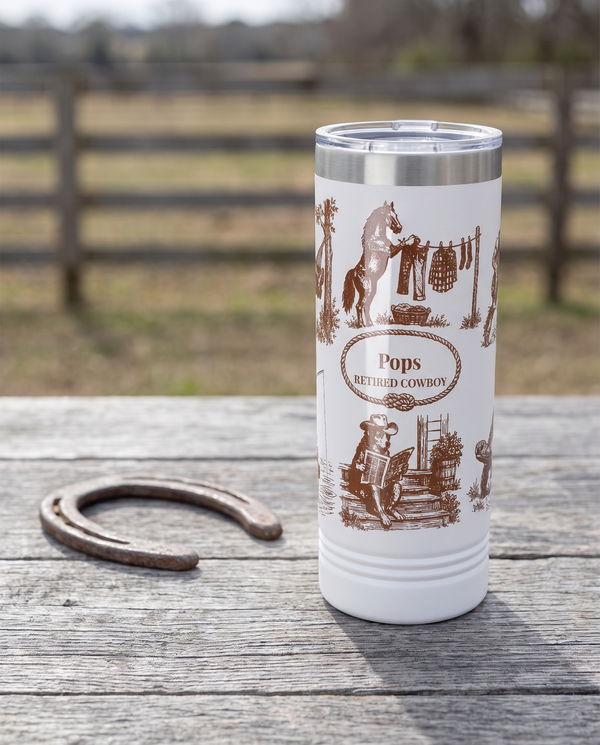 Western Toile, Retired Cowboy wrap on a white 22oz Skinny tumbler personalized POPS, RETIRED COWBOY, a weathered barnwood table on a ranch porch