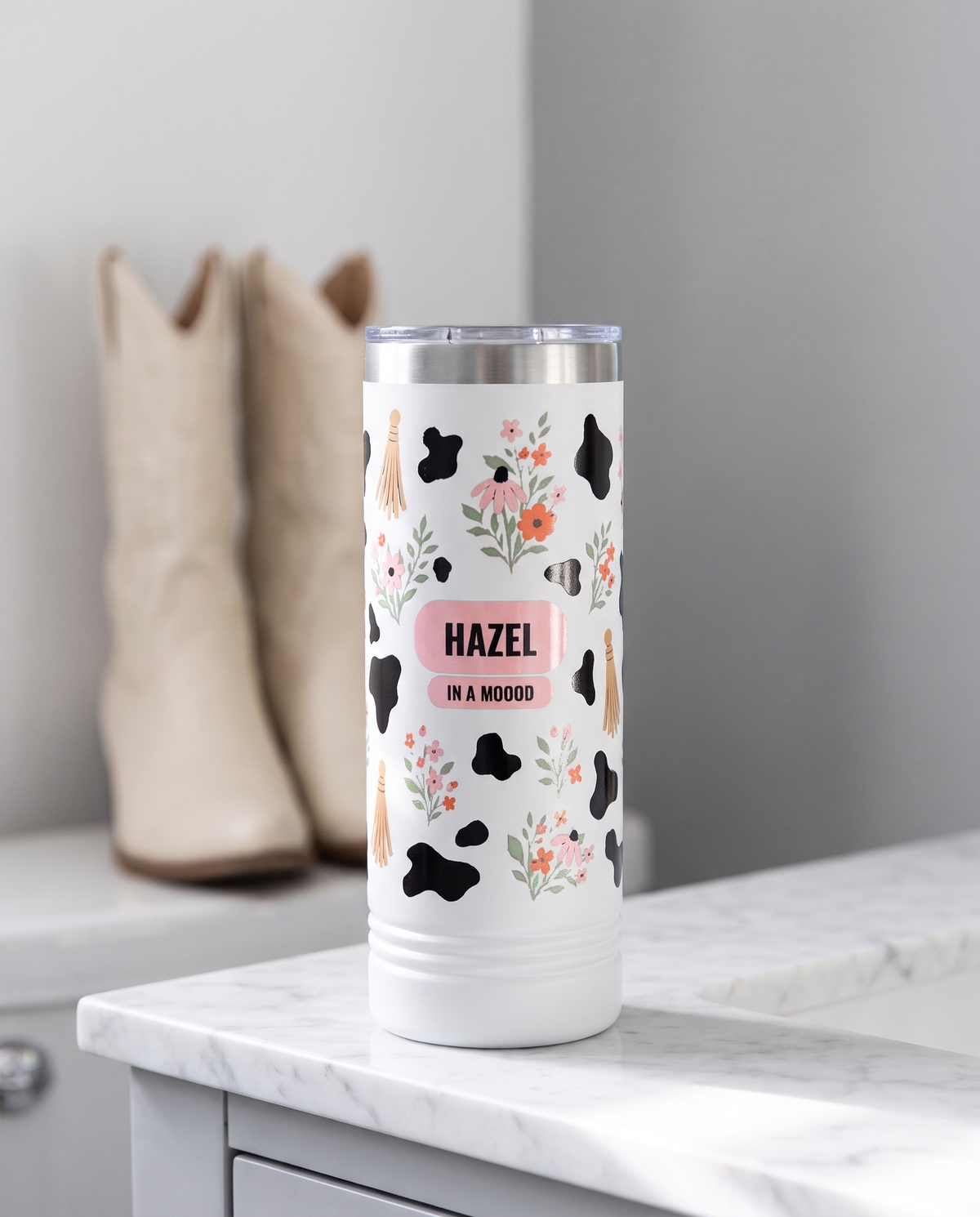 Cow Print Florals, In a Moood wrap on a white 22oz Skinny tumbler personalized HAZEL, IN A MOOOD, a white marble vanity top in a bright boutique