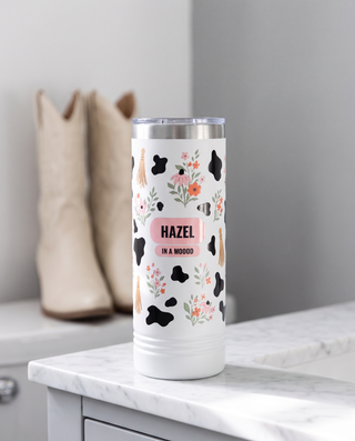 Cow Print Florals, In a Moood wrap on a white 22oz Skinny tumbler personalized HAZEL, IN A MOOOD, a white marble vanity top in a bright boutique