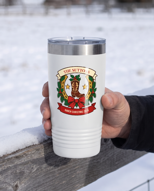 Cowboy Christmas, Horseshoe Wreath badge on a white 20oz tumbler personalized THE SUTTONS, RANCH CHRISTMAS 2026, held in one hand, a snowy fence rail at a ranch