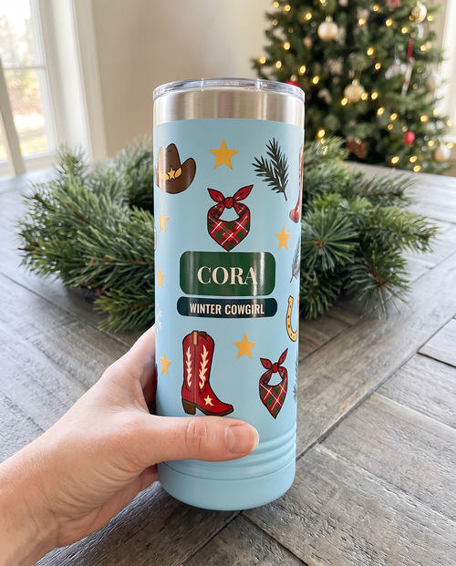 Cowboy Winter, Winter Cowgirl wrap on a light blue 22oz Skinny tumbler personalized CORA, WINTER COWGIRL, held in one hand, a barnwood table in a farmhouse at Christmas