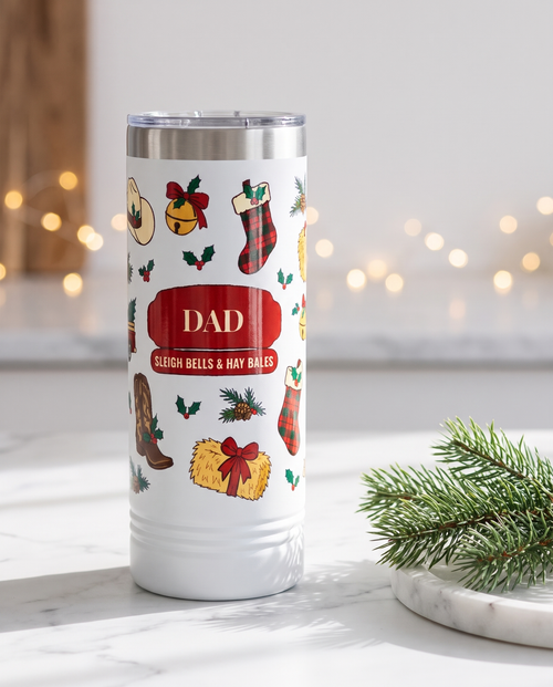 Cowboy Christmas, Sleigh Bells & Hay Bales wrap on a white 22oz Skinny tumbler personalized DAD, SLEIGH BELLS & HAY BALES, a white marble kitchen counter with a sprig of pine