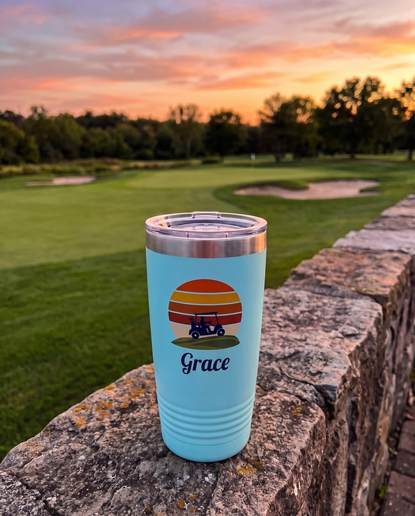 Retro Sunset Cart personalized golf tumbler in light blue on a stone wall by the 18th green at dusk, name Grace