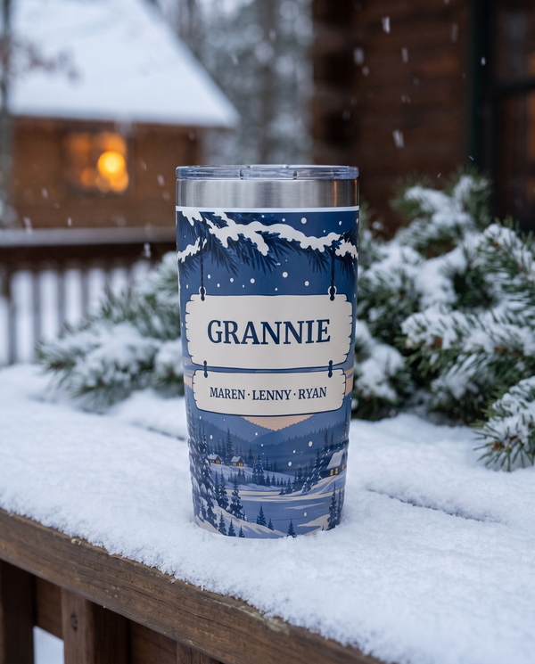 Winter Cardinals, a winter evening scene with cardinals in navy, red, white and cream, printed all the way around a 20oz Ringneck tumbler in White, sample name GRANNIE, sits on a snowy porch table at dusk, evergreen boughs and a lit cabin window far behind