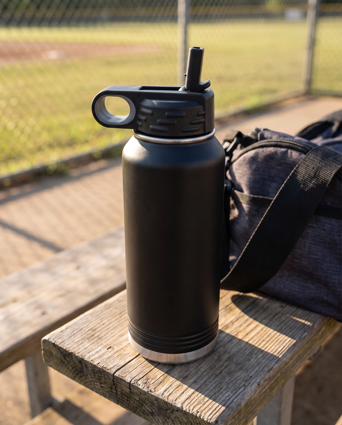 Black flip-top straw lid on a black 32oz water bottle, on a ballpark bench