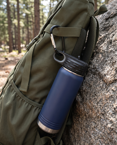 Black carabiner clipping a navy water bottle by its lid loop to a hiking backpack