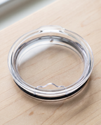 Clear standard lid on its own showing the open sip hole and vent, on a maple board