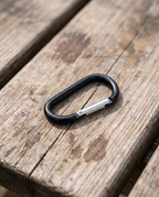 Black carabiner on its own with silver gate, on a picnic table