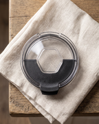 Snap-shut lid on its own from above, black flip cover closed over the front half, on a linen napkin