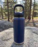 Black lug lid with carry loop on a navy 20oz water bottle, on a granite boulder by a pine trail