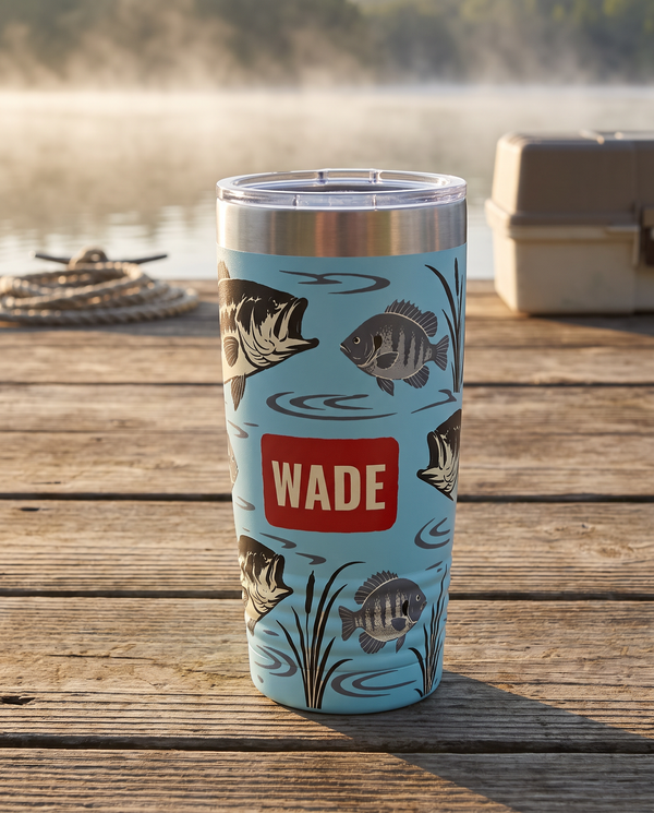Gyotaku Bass and Bluegill art printed all the way around a 20oz Ringneck tumbler in Light Blue, the cup colour showing between the fish, sample name WADE, stands on a lake dock at sunrise