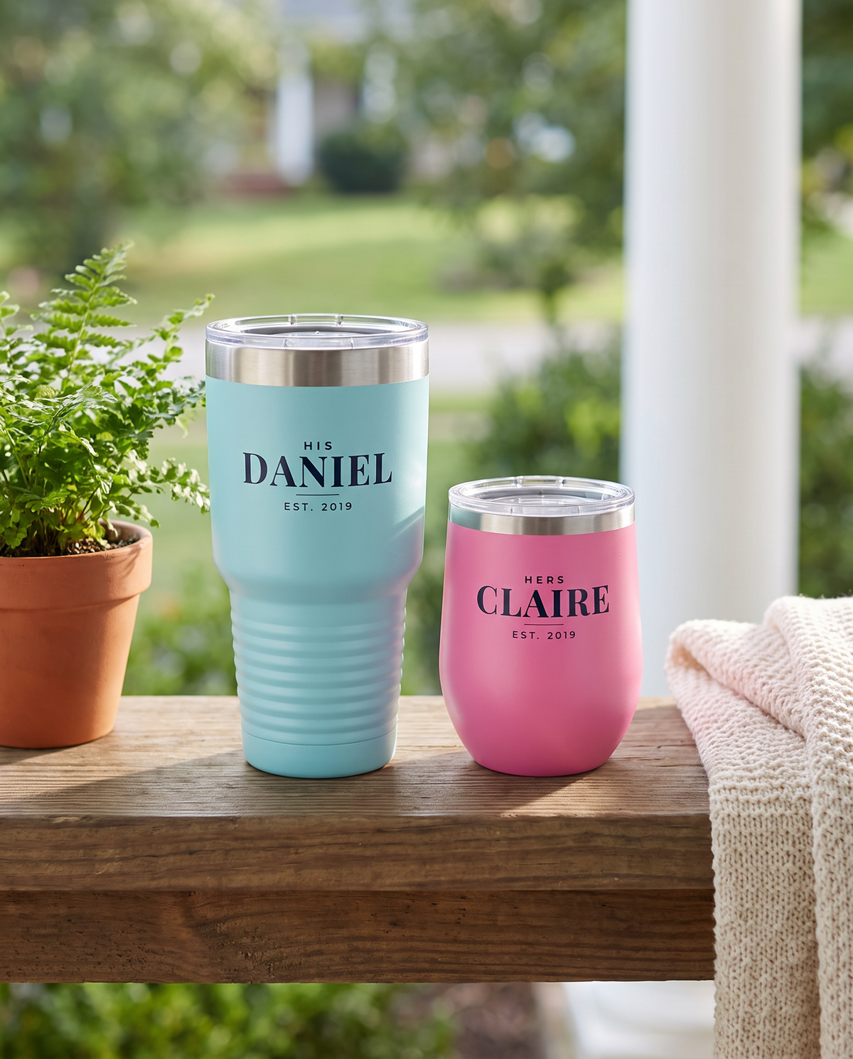 His and hers set: light blue 30oz tumbler named Daniel and pink wine tumbler named Claire on a porch railing