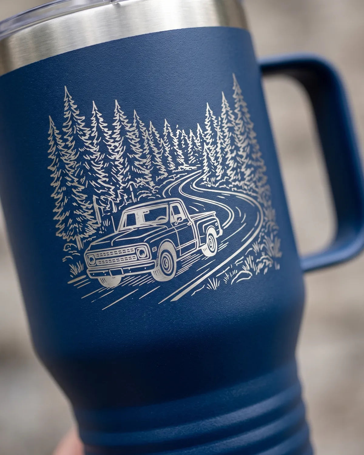 Navy travel mug with an engraved forest and truck scene